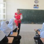 معلم در حال تدریس جلوی تخته سیاه در کلاس درس با دانش‌آموزان نشسته