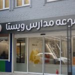 نمای بیرونی درب ورودی مدرسه با تابلوی نام دائمی و لوگو، معماری ساختمان مدرن شامل پنجره‌ها و درهای شیشه‌ای