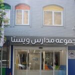 نمای خارجی ساختمان مدرسه با درب ورودی دو لایه، پنجره‌های معماری و تابلوی فارسی، محیط شهری