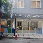 نمای درب ورودی و واجهه خارجی ساختمان مدرسه با پارک ماشین، پنجره‌ها و تابلوی دائمی