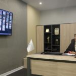 اتاق دفتری اداری با میز پذیرایش، صندلی، نمایشگر ویدیویی روی دیوار و تجهیزات اداری