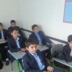 دانش‌آموزان در میز‌های سبز کلاس درس نشسته‌اند و به کلاس توجه می‌کنند