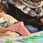 دانش‌آموز در حال انجام فعالیت ساخت‌وساز کاغذی خلاقانه‌ای با همیاری معلم یا والدین