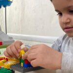 دانش‌آموز دختر در حال ساخت‌وساز با بلوک‌های LEGO رنگین در کلاس فعالیت‌های عملی