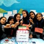 گروهی از دانش‌آموزان دختر در حال شرکت در رویدادی مدرسه‌ای با تزئینات و تابلوهای رنگین در پس‌زمینه