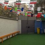 حیاط مدرسه پسرانه علوی امامت با چمن مصنوعی و تزیین پرچم در تهران