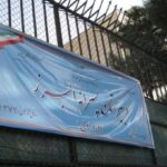 تابلوی نام مدرسه پروانه پرواز بر روی دیوار ساختمان در کنار درب ورودی فلزی