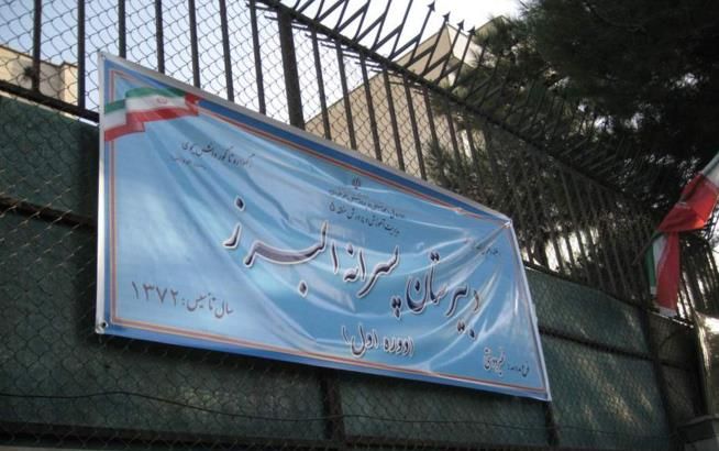 تابلوی نام مدرسه پروانه پرواز بر روی دیوار ساختمان در کنار درب ورودی فلزی