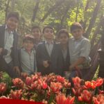 گروهی از دانش‌آموزان در حال شرکت در فعالیت سبزفروشی و عکس‌گرفتن میان گل‌های لاله قرمز و نارنجی در حیاط مدرسه