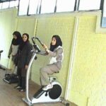 دانش‌آموزان در حال تمرین روی دوچرخه ورزشی ثابت در سالن ورزشی مدرسه