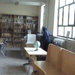 نمای داخلی کتابخانه مدرسه با قفسه‌های کتاب در پس‌زمینه، میز‌های مطالعه و پنجره‌های روشن
