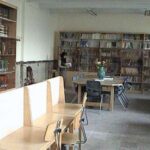 فضای کتابخانه مدرسه با قفسه‌های کتاب گسترده‌ای در دیوار و میز‌های کار چوبی با صندلی‌های فلزی برای مطالعه دانش‌آموزان