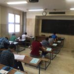 دانش‌آموزانی در حال نوشتن و رسم در یک کلاس درس سنتی با تابلوی سیاه و روشنایی طبیعی