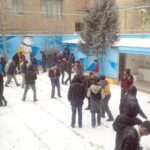 دانش‌آموزان در حیاط مدرسه در حال شرکت در بازی‌های جمعی و فعالیت‌های گروهی در برف
