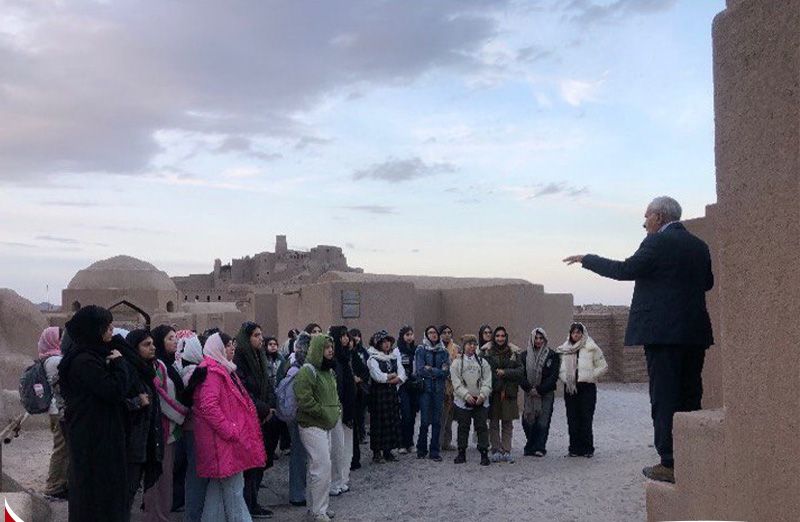 گروهی از دانش‌آموزان در حین بازدید آموزشی به یک بنای تاریخی باستانی با حضور راهنمای گروه