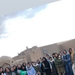 گروهی از دانش‌آموزان پوشیده به لباس‌های فصل سرد، ایستاده در حیاط مدرسه برای عکس جمعی
