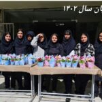 گروه دانش‌آموزان دختر در مراسم جشن پایان سال تحصیلی در کنار سلهای گل‌های رنگین