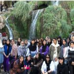 گروهی از دانش‌آموزان دختر، ایستاده در کنار آبشار طبیعی در طول یک تور/رویداد گروهی