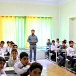 گروه دانش‌آموزان در حال شرکت در یک فعالیت آموزشی گروهی در کلاس درس تحت نظارت معلم