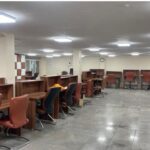 سایت کامپیوتر مدرسه با میز‌های کار و صندلی‌های قرمز رنگ، مجهز به رایانه‌ها و روشنایی‌های سقفی