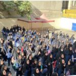 دانش‌آموزان مدرسه در حیاط مدرسه برای شرکت در یک مراسم یا اجتماع گروهی در زیر سایبان‌های قرمز