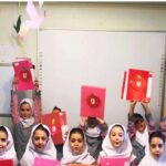 دانش‌آموزان دختر در لباس یکنواخت تحصیلی در مراسم پایانی کلاس، در حال نگاه‌داشتن دفترچه‌های قرمز