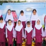 عکس دسته‌جمعی دختران در یونیفرم رسمی کنار دیوار نقاشی‌شده رنگارنگ با تصاویر طبیعت