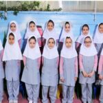 گروهی از دانش‌آموزان دختری با لباس یکسان و روسری سفید در حیاط مدرسه ایستاده‌اند