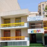نمای خارجی ساختمان مدرسه‌ای با تابلوی مدرسه، درب‌های رنگی زرد و نقاشی‌های رنگی روی دیوار