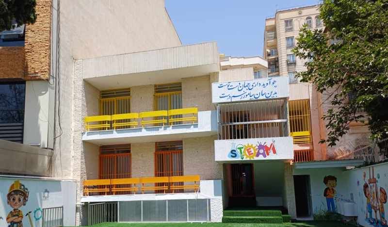 نمای خارجی ساختمان مدرسه‌ای با تابلوی مدرسه، درب‌های رنگی زرد و نقاشی‌های رنگی روی دیوار
