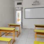 اتاق کلاس درس با میزهای چوبی دارای صفحات زرد و تخته سفید برای نوشتن