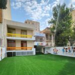 حیاط مدرسه با چمن سبز مصنوعی و بنرهای تعلیمی رنگی برای کودکان