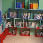 کتابخانه مدرسه با قفسه‌های رنگین آبی و قرمز و سبز پر از کتاب‌های درسی و مرجع