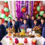 دانش‌آموزان در حال عکس‌گیری گروهی در یک رویداد مدرسه‌ای با تزیینات رنگارنگ، بادکنک‌ها، پارچه‌های بنفش، و نمایش آثار دانش‌آموزان