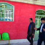 نمای بیرونی ساختمان مدرسه با دیوار قرمز روشن و صندلی‌های رنگی در جلو
