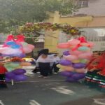 دانش‌آموزان در حیاط مدرسه در حال شرکت در جشن و مراسمی با تزیینات بالون‌های رنگی و لباس‌های سنتی