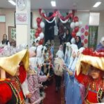 دانش‌آموزان با لباس سنتی رنگی در حین مراسم ایران‌گردی داخل مدرسه، با تزئینات کاغذی قرمز و سفید و شرکت بزرگسالان