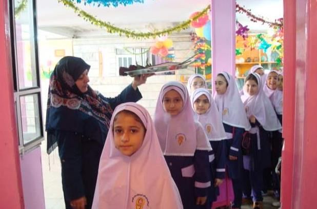 دانش‌آموزانِ پوشش‌دار در حال شرکت در یک فعالیت مراسمی داخل کلاس، با تزیینات موقتِ رنگی و راهنمایی یک معلم