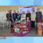 تصویری از یک مراسم خیری در حیاط مدرسه با حضور معلمان و مسئولین و میزهای نمایشی برای فروخت خیری