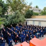 تجمع دسته‌جمعی دانش‌آموزان دختر با لباس‌های آبی رنگ در حیاط مدرسه برای شرکت در یک مراسم یا فعالیت گروهی