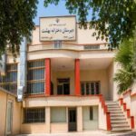 نمای خارجی ساختمان مدرسه با درب ورودی، تابلوی نام‌نویسی و طراحی معماری کلاسیک ایرانی