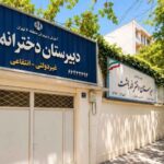 نمای بیرونی درب ورودی و سردر ساختمان مدرسه با تابلوی نام و درب‌های فلزی
