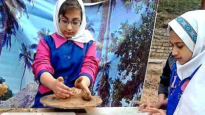 دو دانش‌آموز دختر در حال انجام یک پروژه‌ی عملی با خاک یا مواد خاکی در محیطی مدرسه‌ای