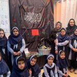 گروهی از دانش‌آموزان دختر و معلم در حال شرکت در مراسم یادبود جمعی با تزیینات و نمادهای مذهبی