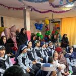 دانش‌آموزان دختر با لباس‌های مدرسه‌ای در حال شرکت در مراسم جشن مدرسه با تزئینات بادکنک و پوسترهای رنگی
