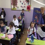 دانش‌آموزان در کلاس درسی مجهز به میزهای سبز رنگ، دیوارهای بنفش و دکوریشن‌های آموزشی، در حال انجام فعالیت‌های درسی