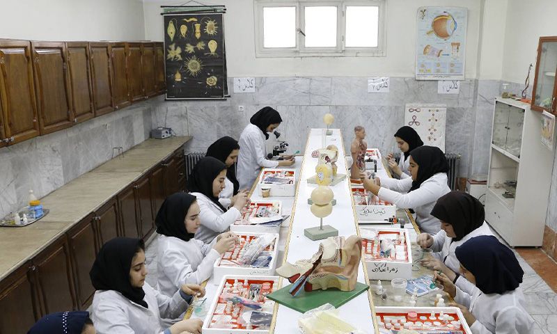 دانش‌آموزان دختر در حال انجام آزمایش علمی در آزمایشگاه مدرسه، با ابزار و مواد آزمایشگاهی روی میز
