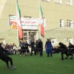 دانش‌آموزان در حال شرکت در یک فعالیت ورزشی جمعی در سالن ورزشی مدرسه با درهای ورودی و تابلوهای رسمی در پس‌زمینه