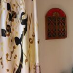 گوشه‌ای از راهروی داخلی مدرسه با دیوار کرم‌رنگ، پرده تزیینی با الگوی هندسی، چهارچوب قرمز روی دیوار و ابزارهای تمیز‌کاری