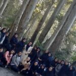 گروهی از دانش‌آموزان لباس‌های رسمی پوشیده، برای عکس یادتی جمع‌شده در حیاط ساختمان میان درختان راش.